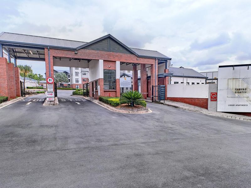 The secure entrance gatehouse of the Canvas Eighty2 apartment complex, featuring brick construction, controlled access points, and professional landscaping.