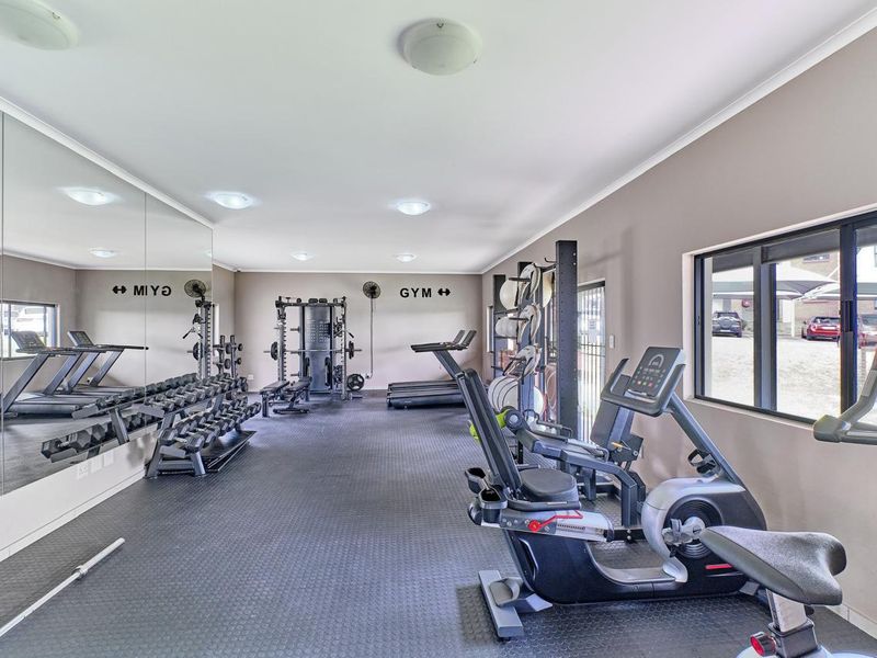 A well-maintained private gym featuring mirrored walls, durable rubberized flooring, and recessed lighting, providing a functional space for fitness activities.