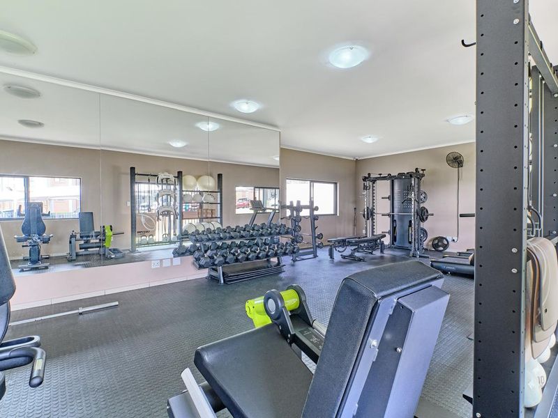 A dedicated home gym featuring wall-to-wall mirrors, durable rubberized flooring, and recessed lighting, providing a functional space for fitness and exercise.