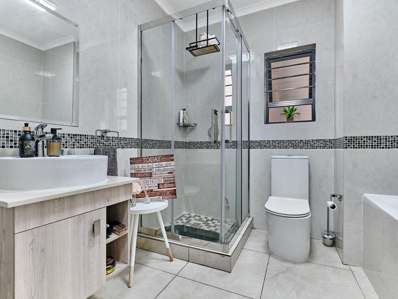 Modern bathroom featuring a glass shower enclosure, vessel sink with vanity cabinet, bathtub, and neutral tiled finishes with a decorative mosaic border.