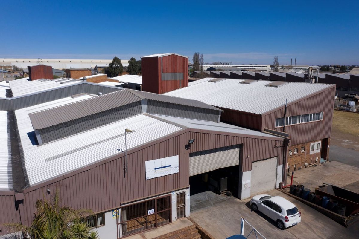 Aerial view of an industrial warehouse facility featuring corrugated metal roofing, large roller shutter access, and integrated skylights within a commercial estate setting.
