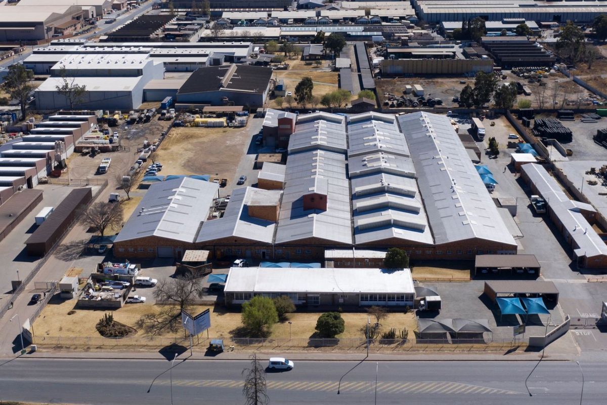 Aerial view of a large industrial warehouse complex featuring extensive corrugated metal roofing, sawtooth design, and dedicated parking areas with shade structures.