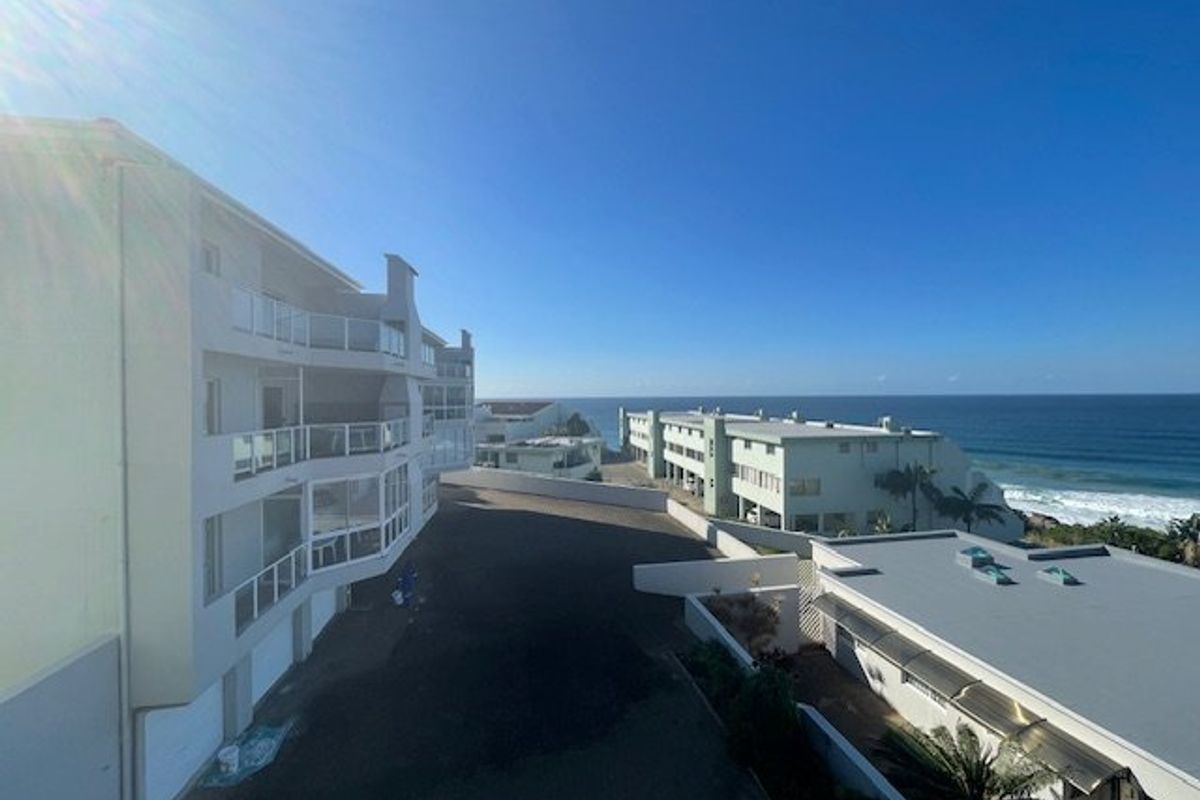 An elevated aerial view of the apartment complex exterior, showcasing the building architecture, balconies, and proximity to the ocean.