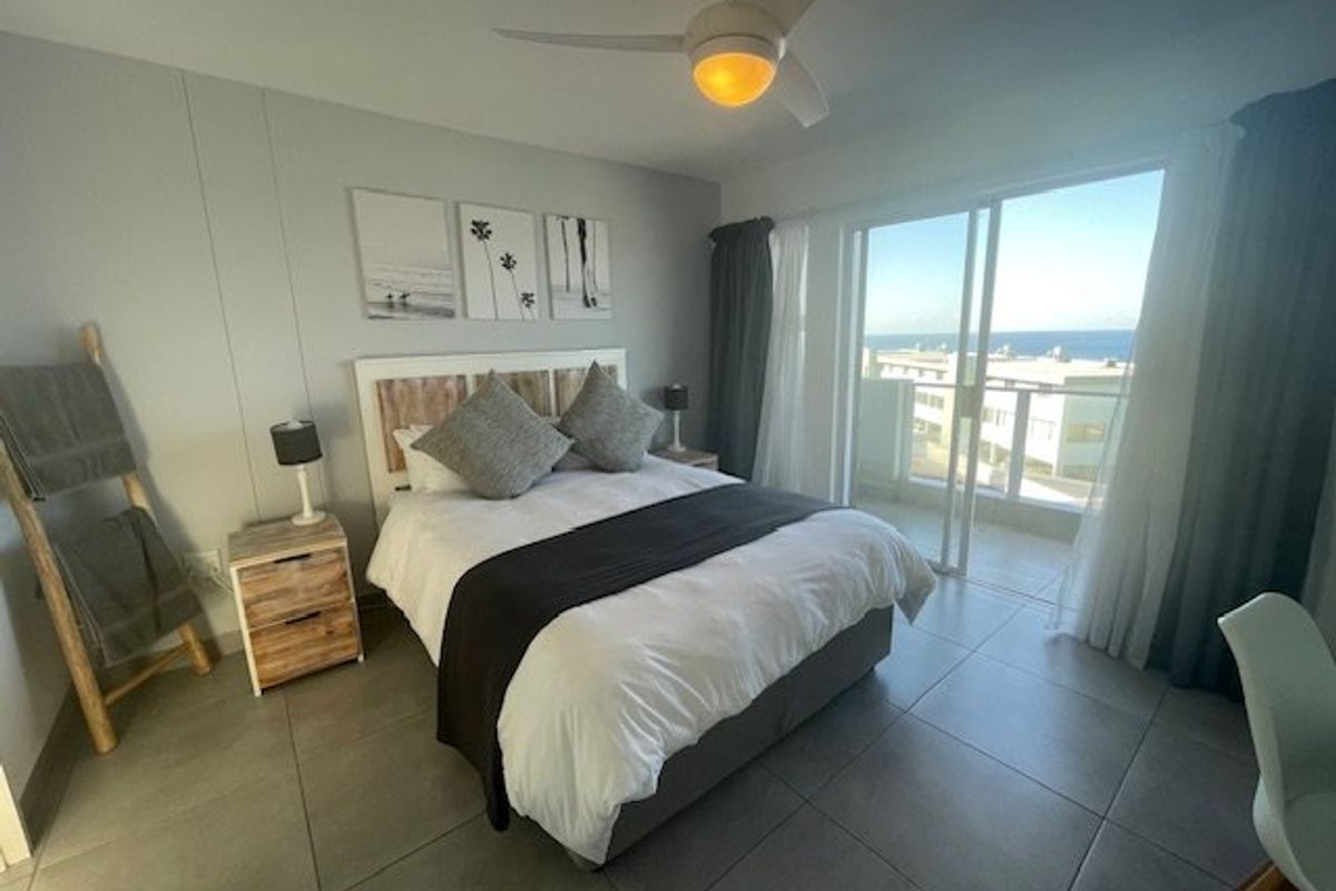 A well-maintained bedroom featuring tiled flooring, a ceiling fan, and sliding glass doors that open onto a balcony with ocean views.