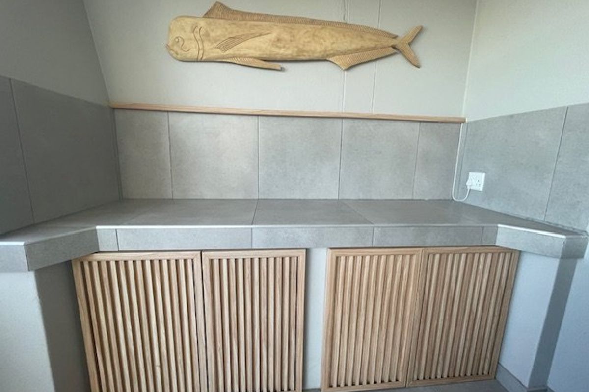 A clean kitchen prep area featuring tiled countertops, a tiled splashback, and custom slatted timber cabinetry.