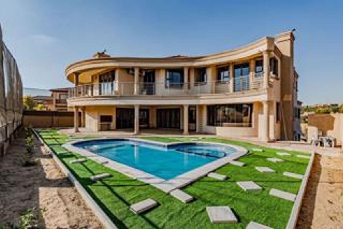 A spacious rear exterior view featuring a curved architectural design, a swimming pool, a covered patio, and an upper-level balcony.