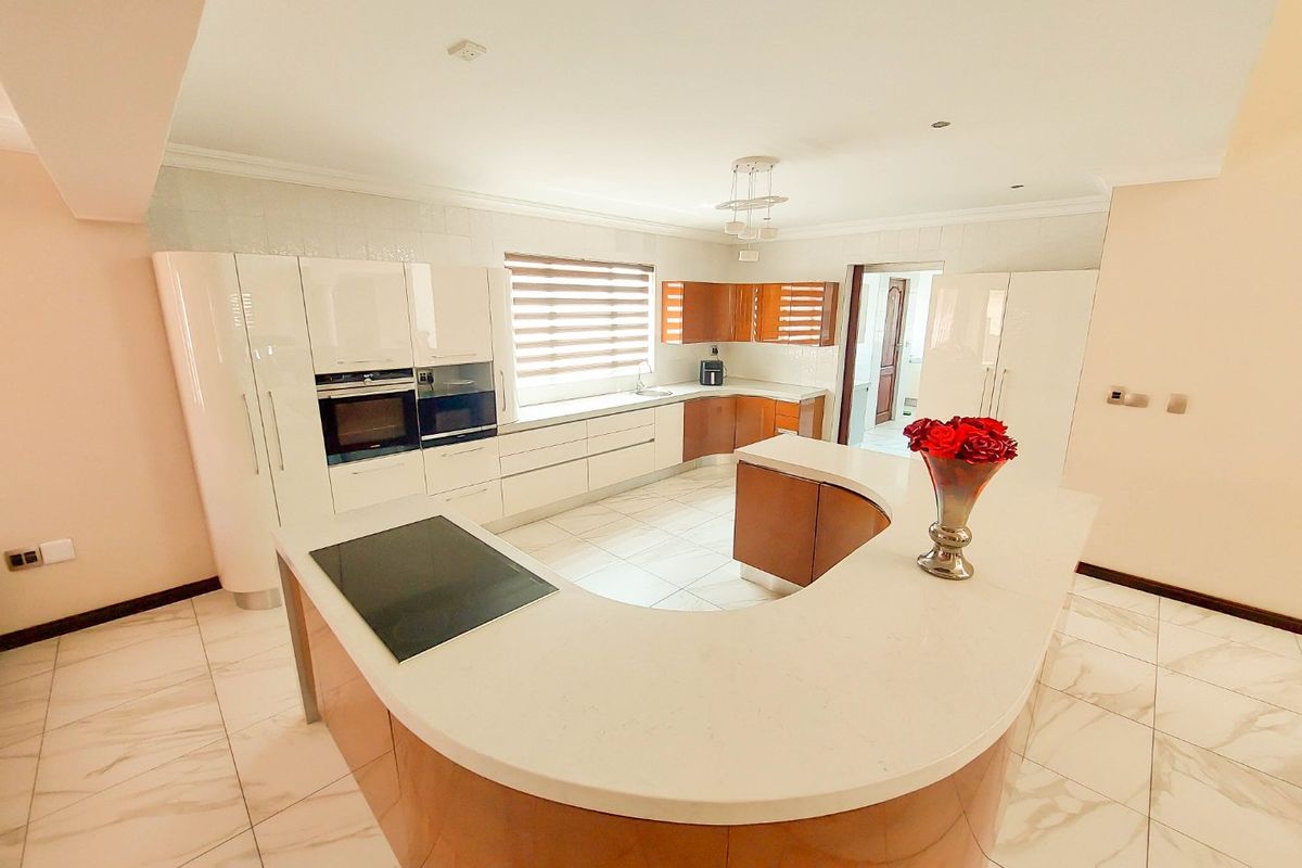 Modern kitchen featuring a curved island with stone countertops, built-in appliances, high-gloss cabinetry, and light-toned tiled flooring.