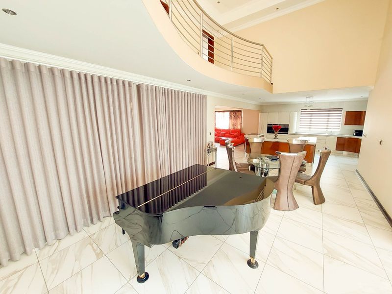 Spacious open-plan living area featuring a double-volume ceiling, mezzanine level with stainless steel balustrade, marble-look flooring, and a modern integrated kitchen.