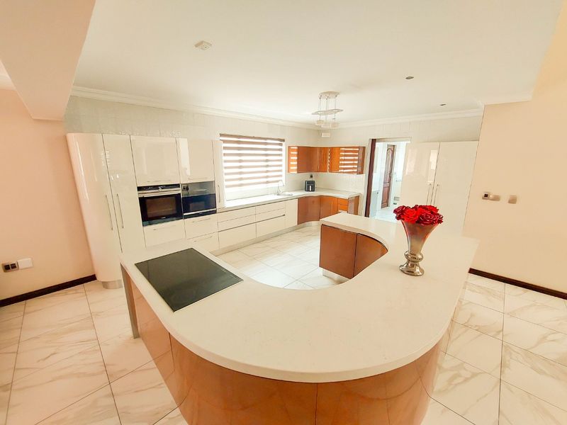 Modern kitchen featuring a curved island with stone countertops, built-in oven, microwave, induction hob, and high-gloss cabinetry with tiled flooring.