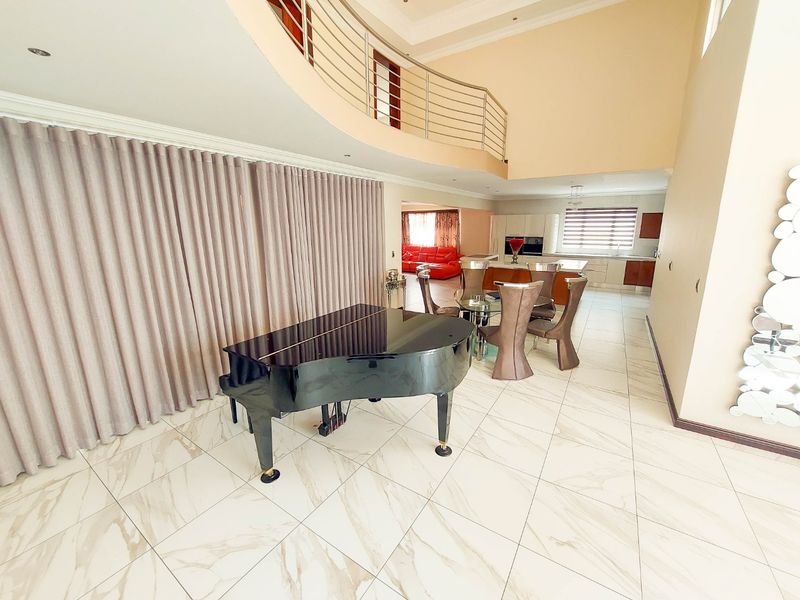 Spacious open-plan living area featuring high ceilings, a mezzanine level with stainless steel balustrade, marble-look tiled flooring, and a modern integrated kitchen.