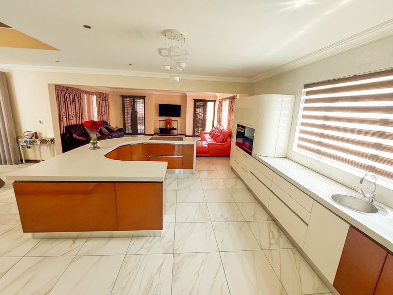 Spacious open-plan living area featuring a modern kitchen with a large U-shaped island, integrated appliances, and sleek marble-look tiled flooring throughout.