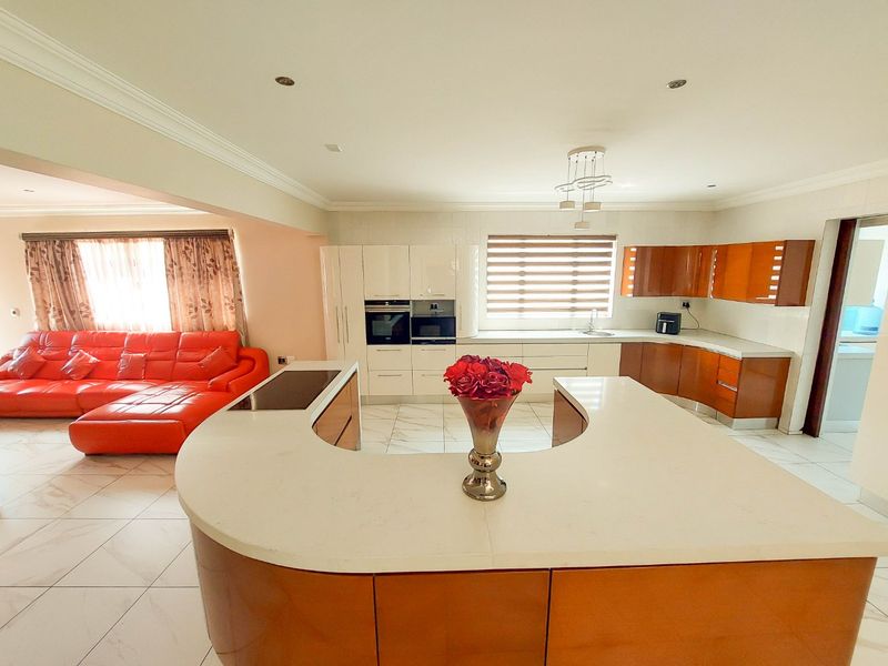 Spacious open-plan kitchen and living area featuring a curved island with stone countertops, built-in appliances, and modern tiled flooring.