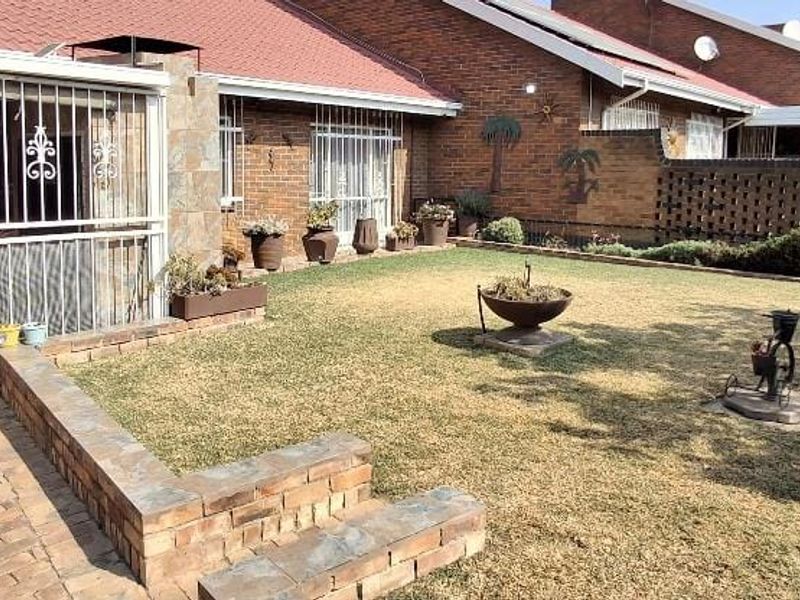 A rear exterior view of a townhouse featuring a brick-paved patio area, a small lawn, and a brick facade with security-fitted windows and doors.