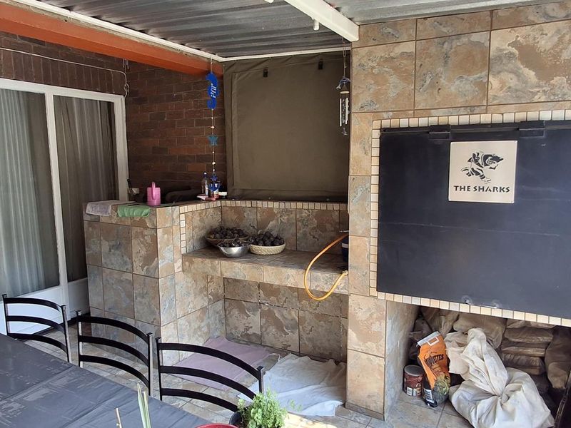 Covered patio area featuring a built-in braai with tiled finishes and direct access to the interior through sliding glass doors.