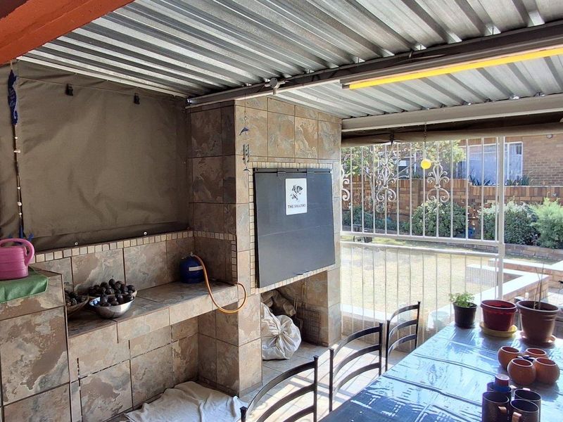 Covered patio area featuring a built-in braai with tiled finishes, corrugated metal roofing, and direct access to the garden through a security gate.
