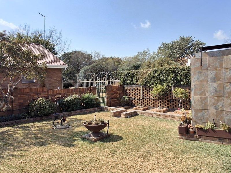 A private rear garden featuring a lawn, brick boundary walls, security fencing, and a tiled feature wall attached to the townhouse structure.