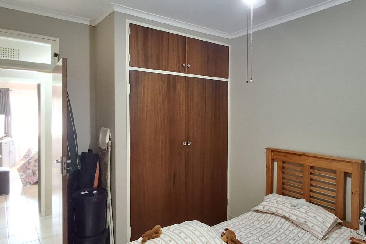 A bedroom featuring a built-in wooden wardrobe, neutral wall finishes, and a doorway leading to an adjacent room.