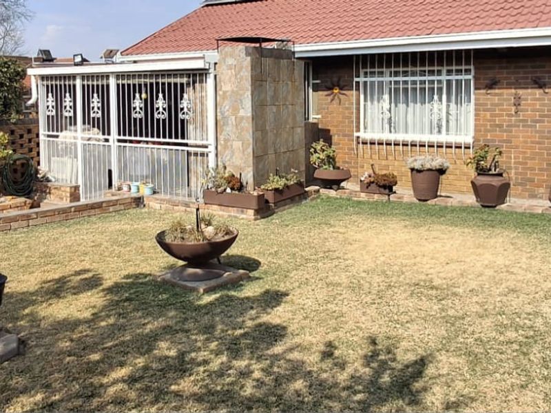 A private rear garden featuring a brick facade, security-barred windows, a stone-clad chimney, and established raised brick garden beds.