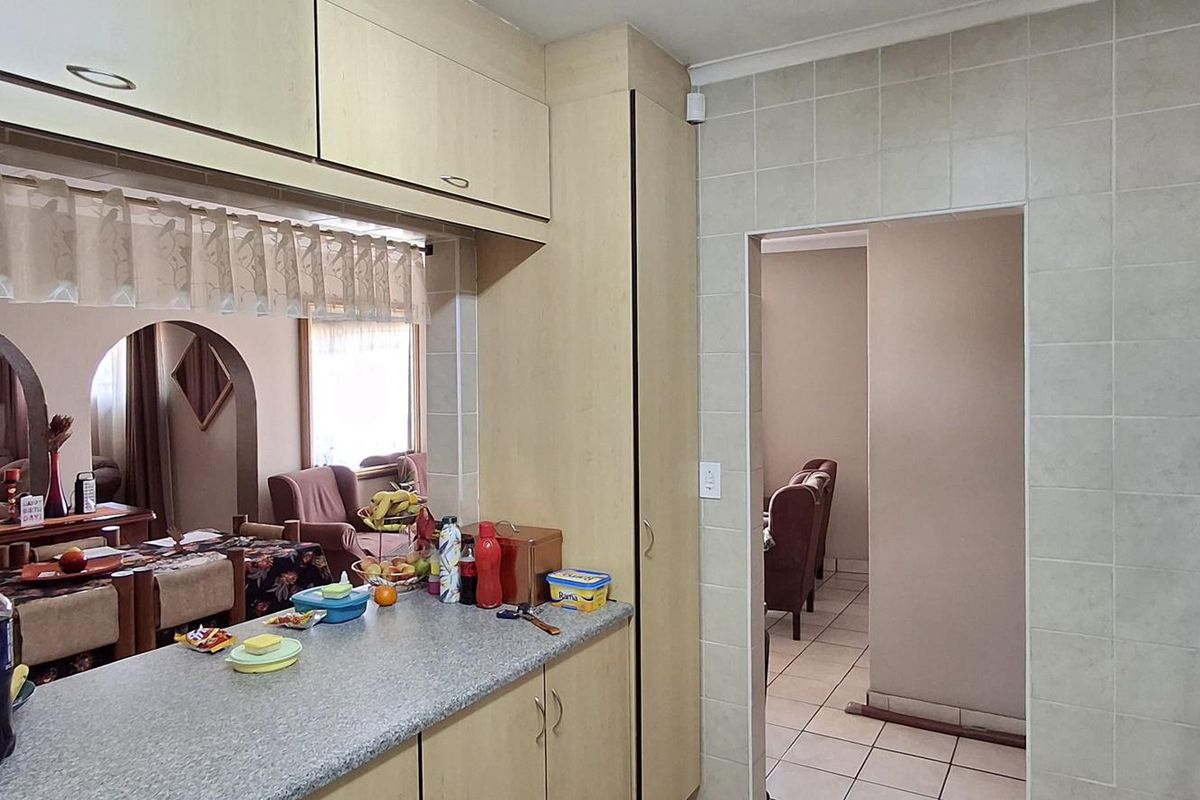 A functional kitchen featuring laminate cabinetry, tiled splashbacks, and a convenient pass-through window connecting to the adjacent living and dining areas.