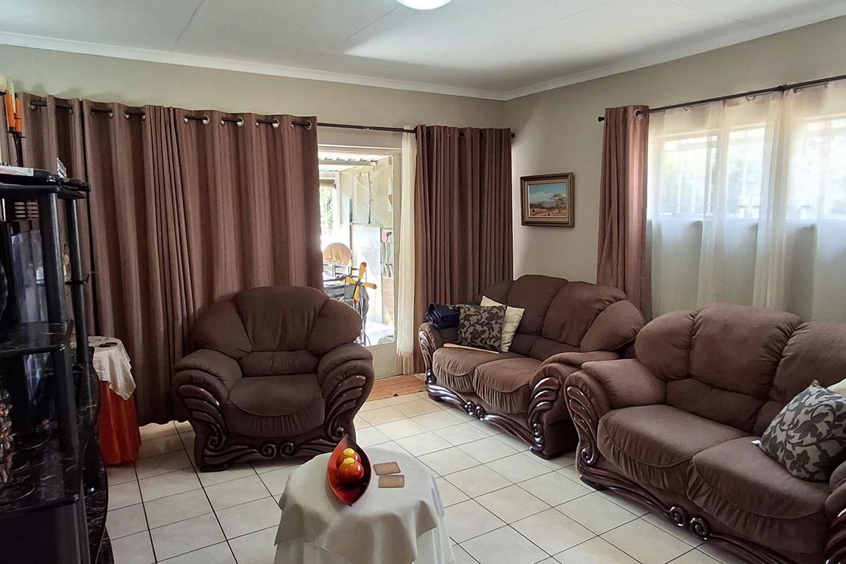 A comfortable living room featuring tiled flooring, large windows with security bars, and direct access to an outdoor area.