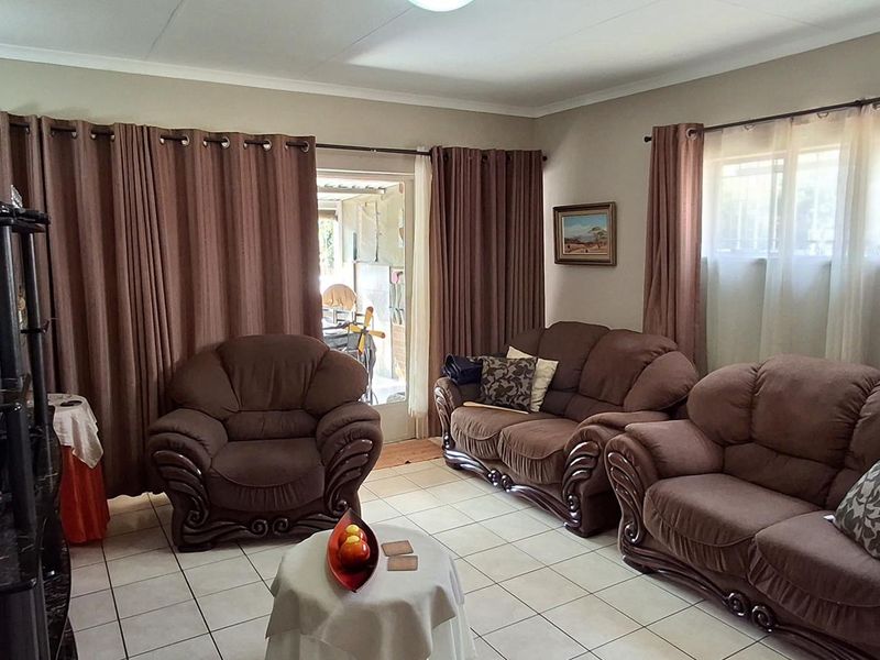 A comfortable living room featuring tiled flooring, large windows with security bars, and direct access to an outdoor area.