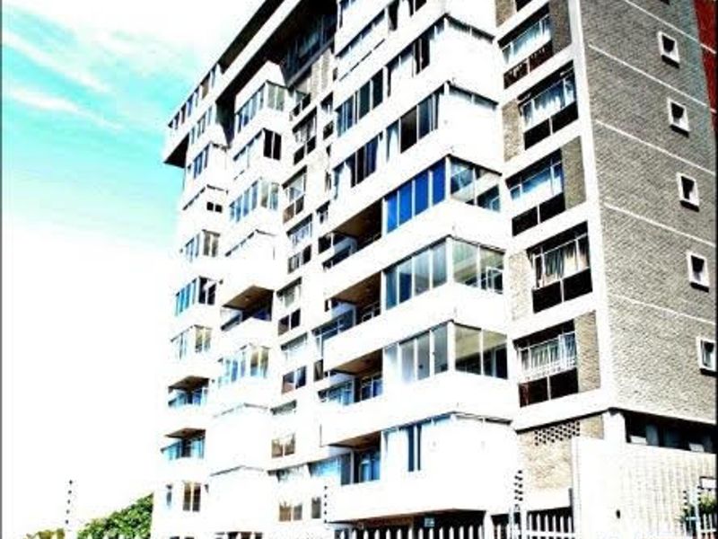 A multi-story apartment building featuring a brick facade, multiple balconies, and secure perimeter fencing.