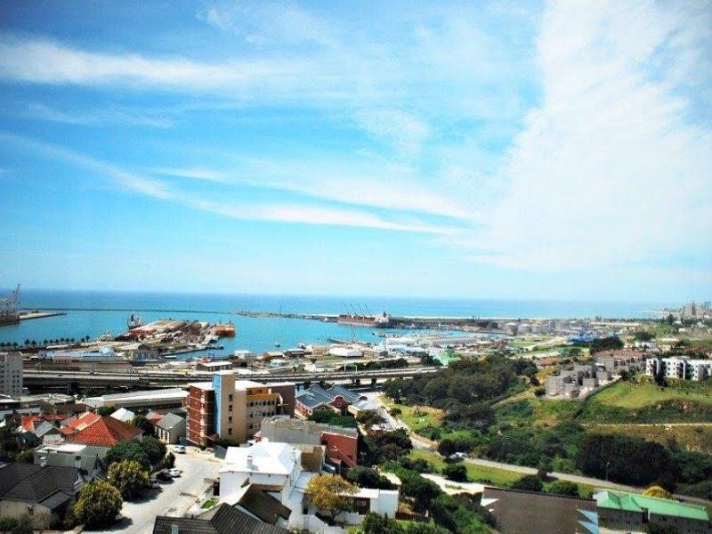 An elevated panoramic view overlooking the coastal harbor, industrial port area, and surrounding urban landscape.