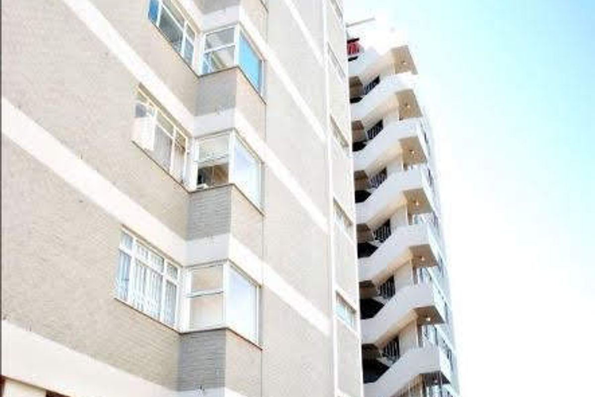A view of the multi-story apartment building exterior, featuring an external staircase and perimeter security fencing.