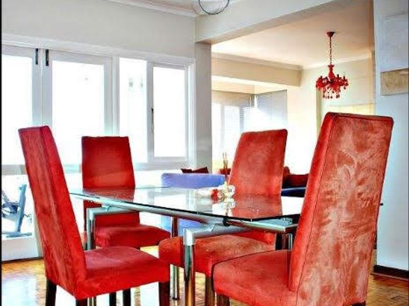 A bright dining area featuring warm parquet flooring, large windows for natural light, and a modern pendant light fixture.