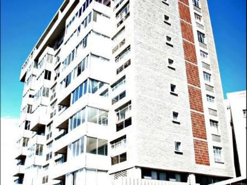 Exterior view of a multi-story apartment building featuring a brick facade, balconies, and secure perimeter fencing.