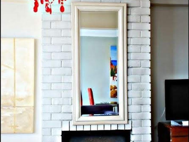 A living room featuring a white painted brick fireplace with a hearth and crown molding, complemented by hardwood flooring.