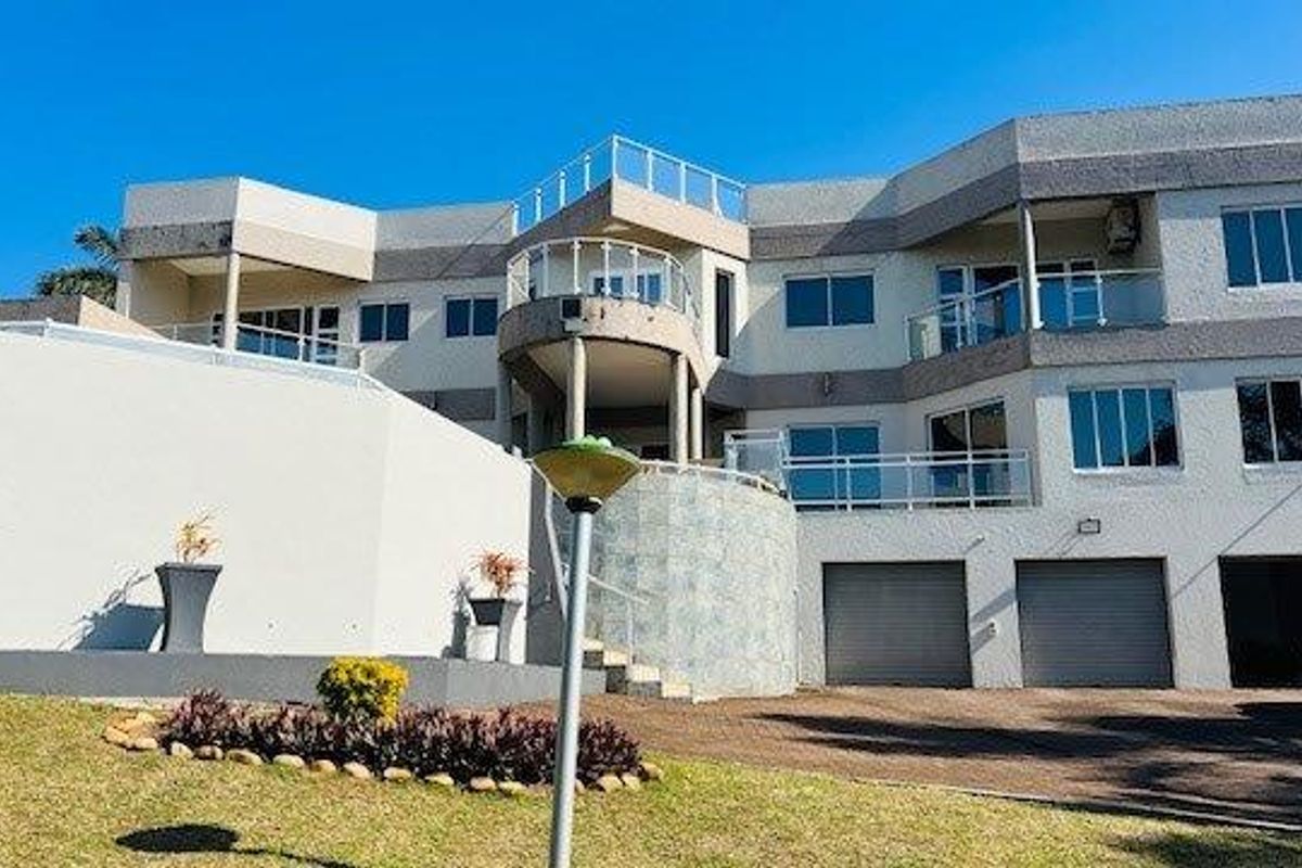 A multi-level rear elevation of a large residential property featuring extensive balconies with glass balustrades, a triple garage, and a paved driveway area.