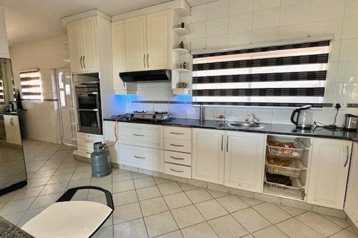 A functional kitchen featuring white cabinetry, a double wall oven, gas hob, and tiled finishes throughout.