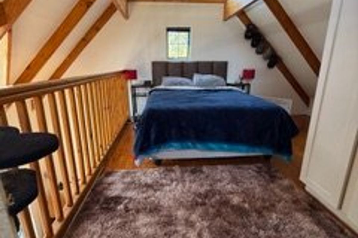 A loft-style bedroom featuring exposed timber rafters, a wooden balustrade, and warm timber flooring, creating a cozy and rustic atmosphere.