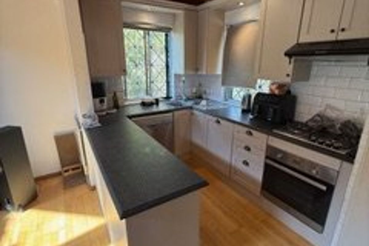 A functional kitchen featuring warm timber ceiling beams, stone countertops, subway tile backsplash, and integrated appliances with hardwood flooring throughout.