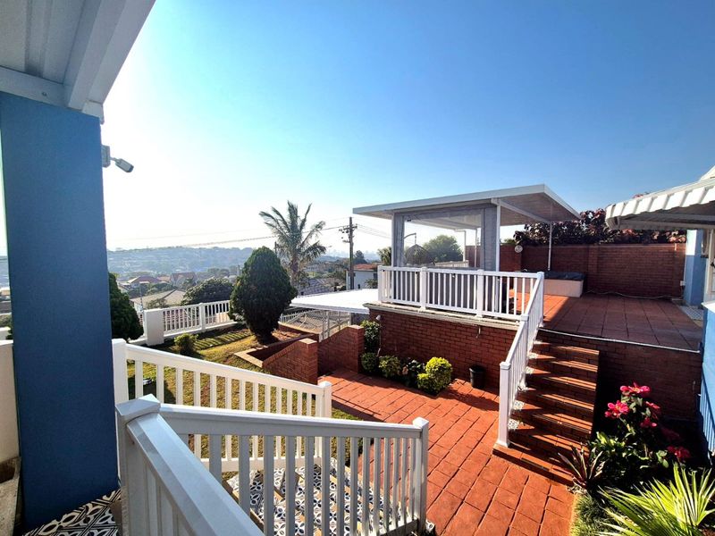 A multi-level outdoor patio area featuring brick paving, white balustrades, and a covered entertainment space with elevated views of the surrounding neighborhood.