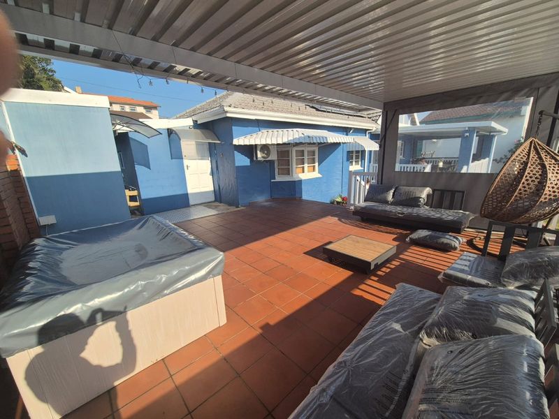 Covered outdoor patio featuring terracotta tiling, a built-in spa, and protective roller blinds, providing a functional space for outdoor relaxation.