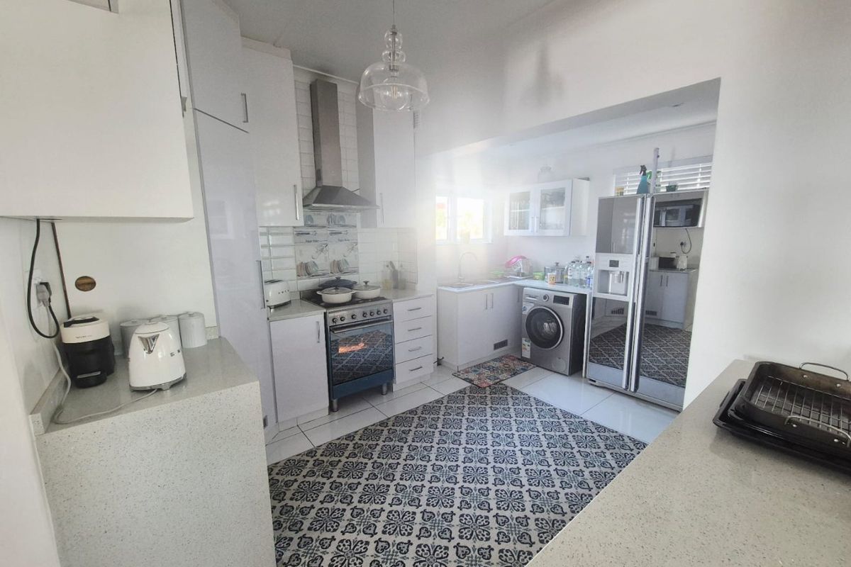 A functional kitchen featuring white cabinetry, stone countertops, stainless steel oven with extractor fan, and integrated laundry space with tiled flooring.