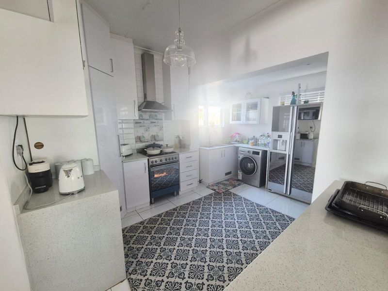 A functional kitchen featuring white cabinetry, stone countertops, stainless steel oven with extractor fan, and integrated laundry space with tiled flooring.