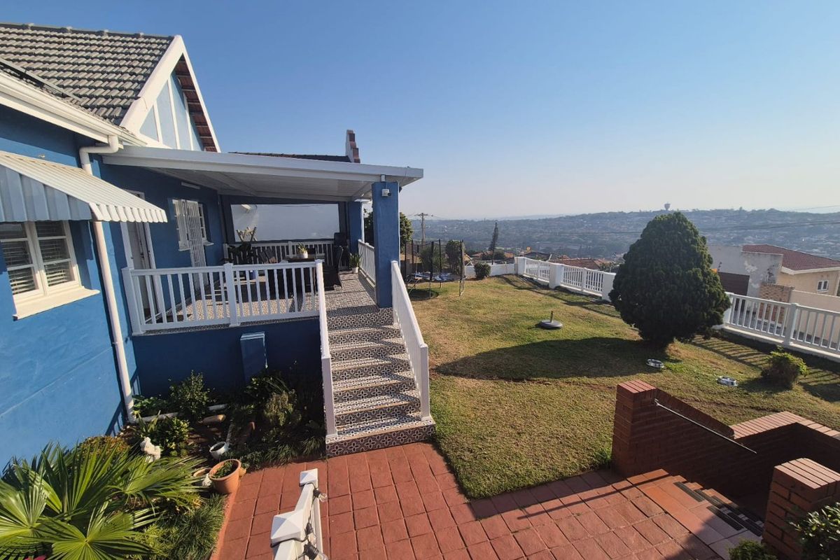 Rear exterior view featuring a covered patio, tiled staircase, brick paved area, and a well-maintained garden with expansive elevated views.