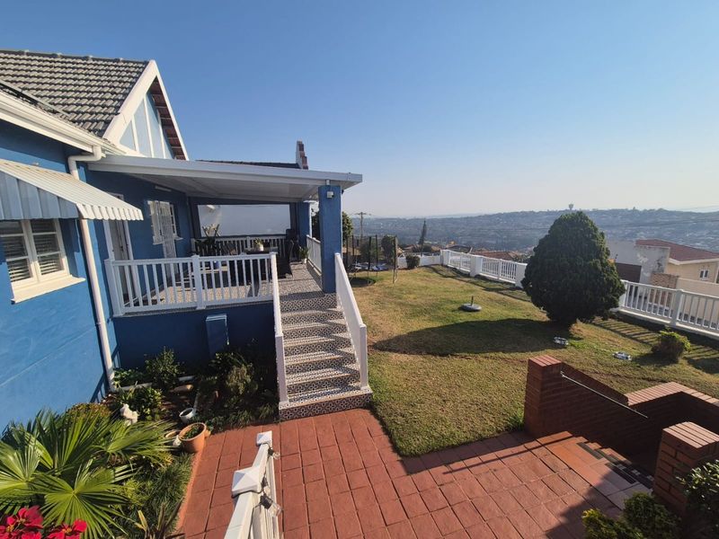 Rear exterior view featuring a covered patio, tiled staircase, brick paved area, and a well-maintained garden with expansive elevated views.