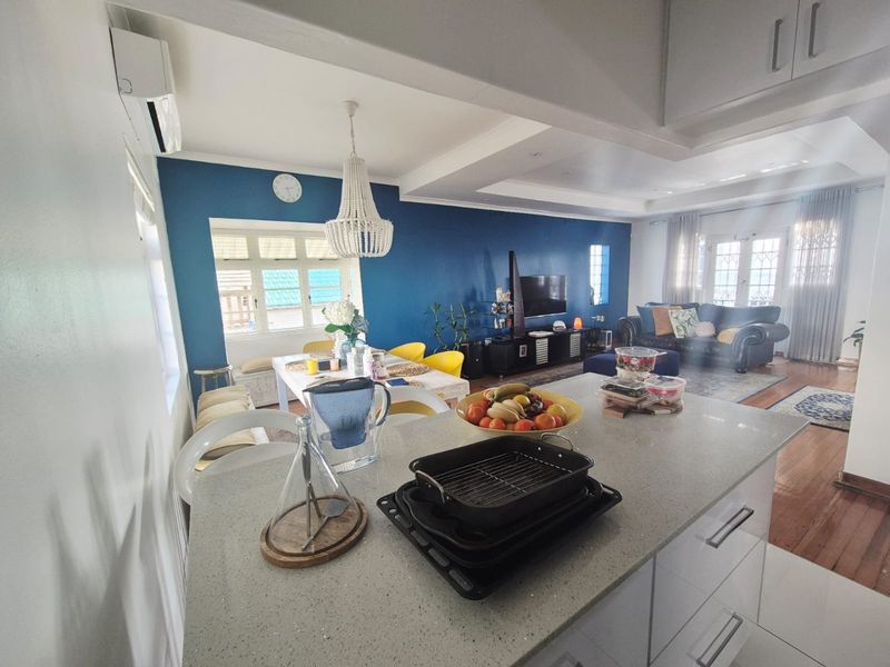 Spacious open-plan living and dining area featuring a central kitchen island with stone countertops, hardwood flooring, and a modern split-system air conditioner.