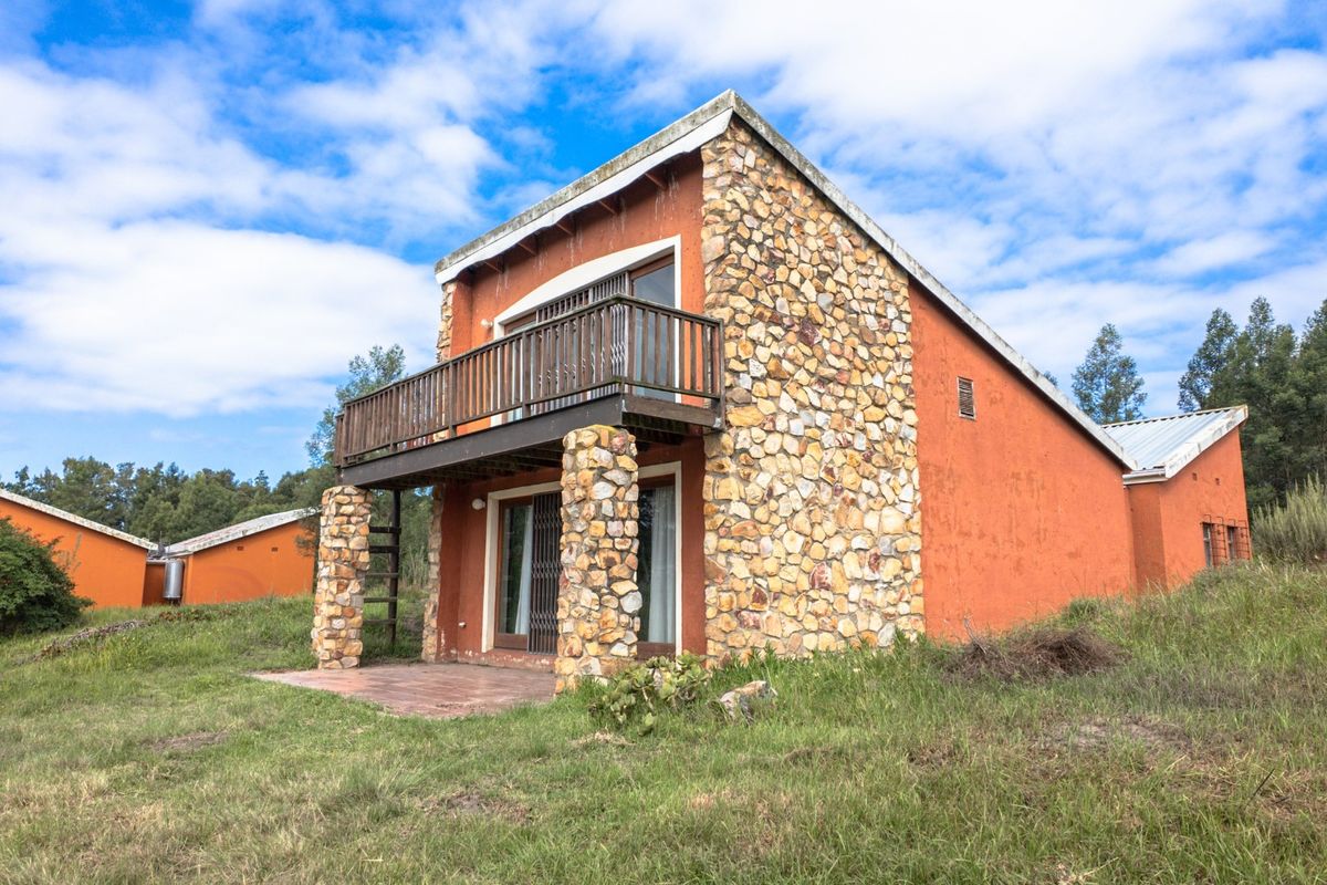 A rustic farm-style dwelling featuring stone cladding, a private balcony, and a ground-level tiled patio set within a natural landscape.