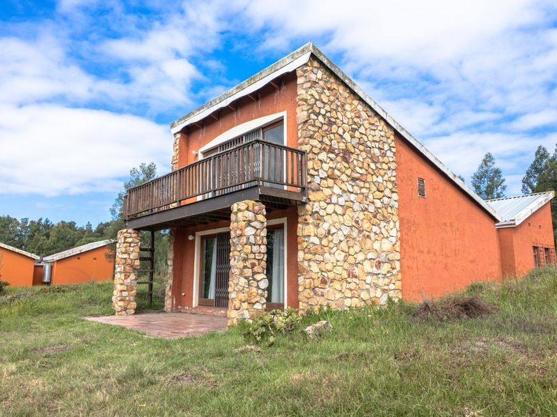 A rustic farm-style dwelling featuring stone cladding, a private balcony, and a ground-level tiled patio set within a natural landscape.