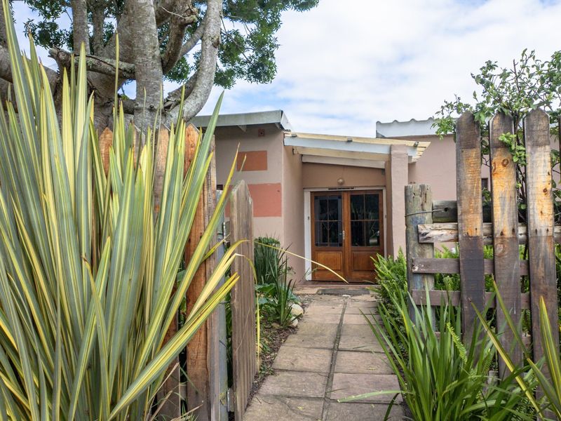 Front entrance of the farm property featuring a paved walkway, timber fencing, and double wooden doors under a simple skillion roof structure.