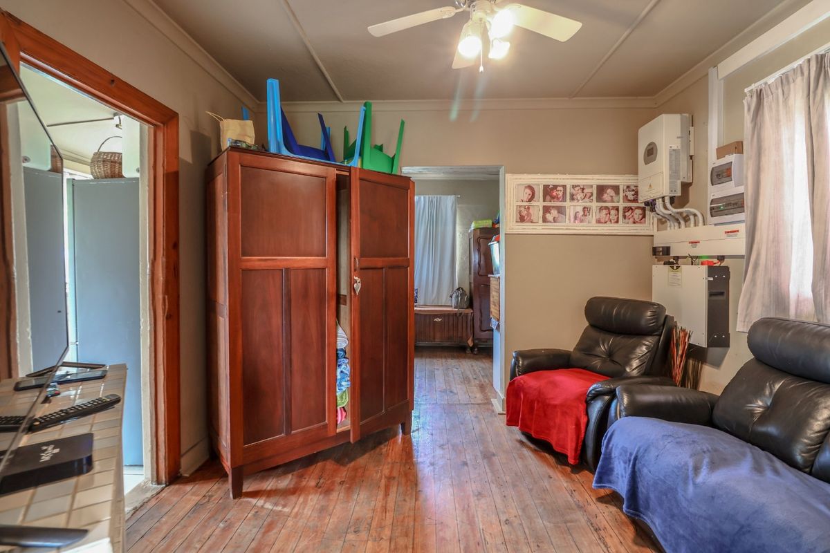 A living room featuring original hardwood flooring, a ceiling fan, and a wall-mounted inverter system for power backup.