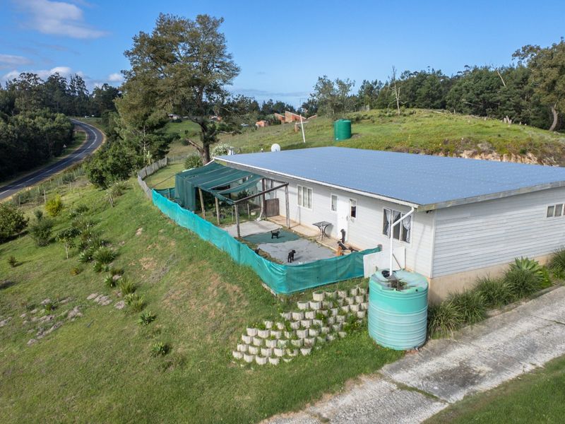 Aerial view of a farm property featuring a single-story dwelling with a metal roof, water storage tanks, and a covered patio area.