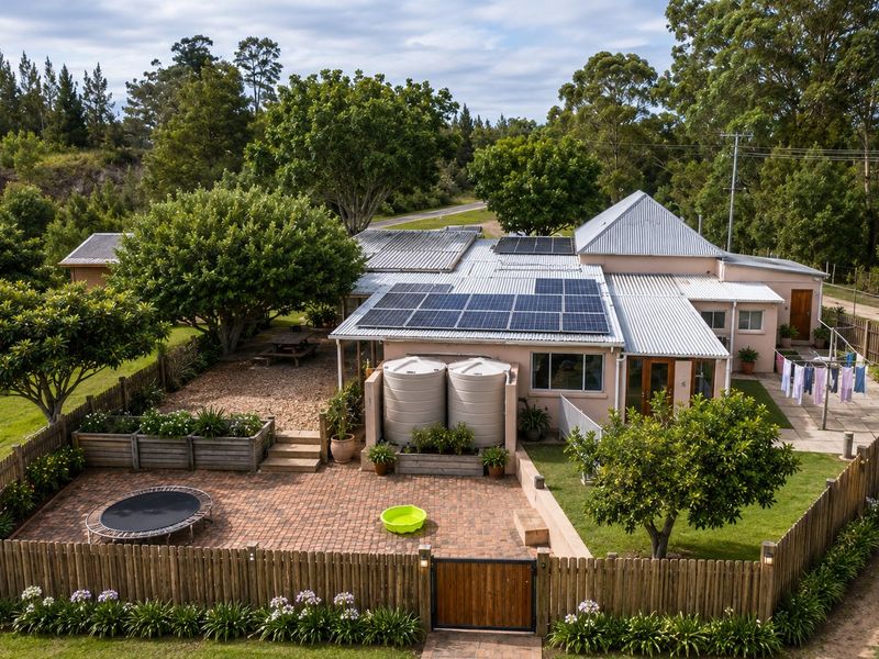 Aerial view of a farm property featuring a residence with solar panels, water tanks, a brick-paved patio, and established garden areas.