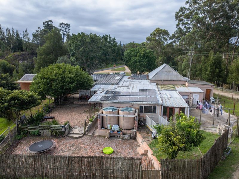 Aerial view of a farm property featuring a main dwelling with solar panels, water storage tanks, and a brick-paved rear courtyard area.