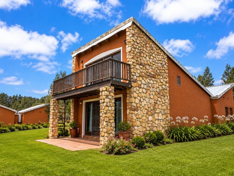 A well-maintained farm-style building featuring stone cladding, a private balcony, and a ground-floor patio overlooking a lush green lawn.